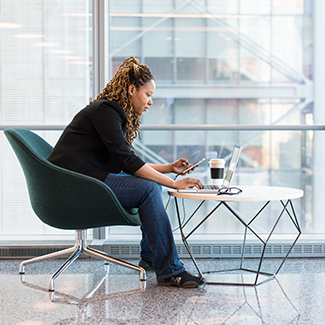 Woman sitting at a small table with her laptop in an office