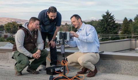 Three men examine a pollen monitor on top of a roof.