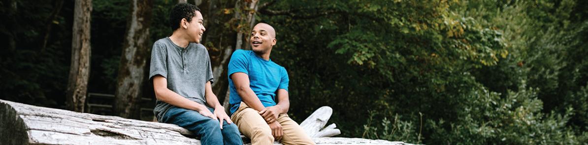 Two people sitting on a log in nature and talking.