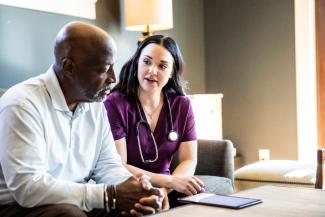 Medical provider in plum colored shirt reviewing medical information with patient in white shirt.